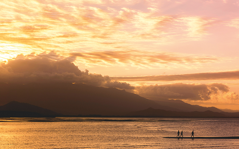 Three people walking by the water at sunset