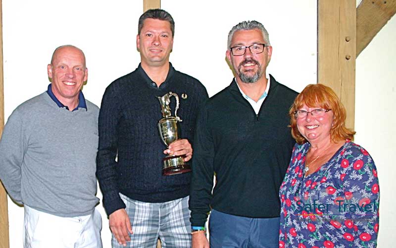 Three men and one woman smiling posing with golf trophy