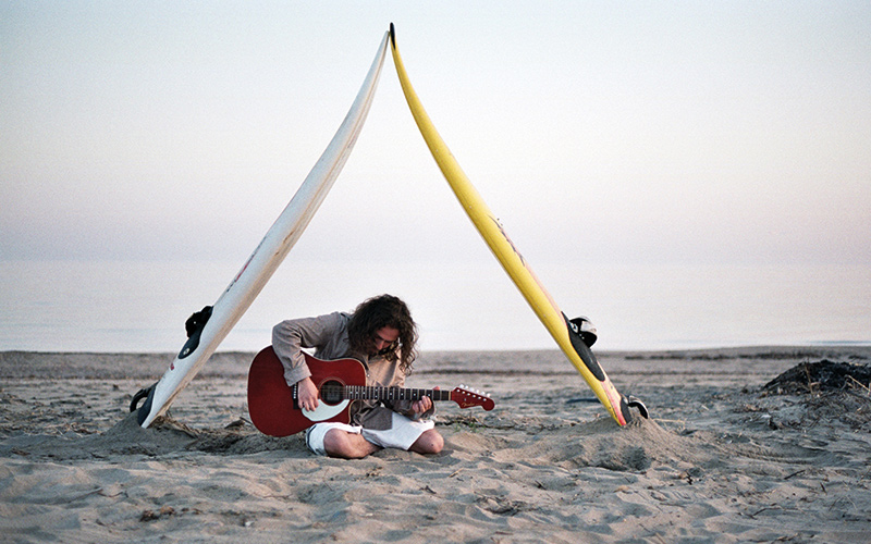 Playing guitar on beach under surf boards