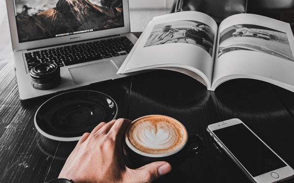 Person drinking coffee on laptop and book